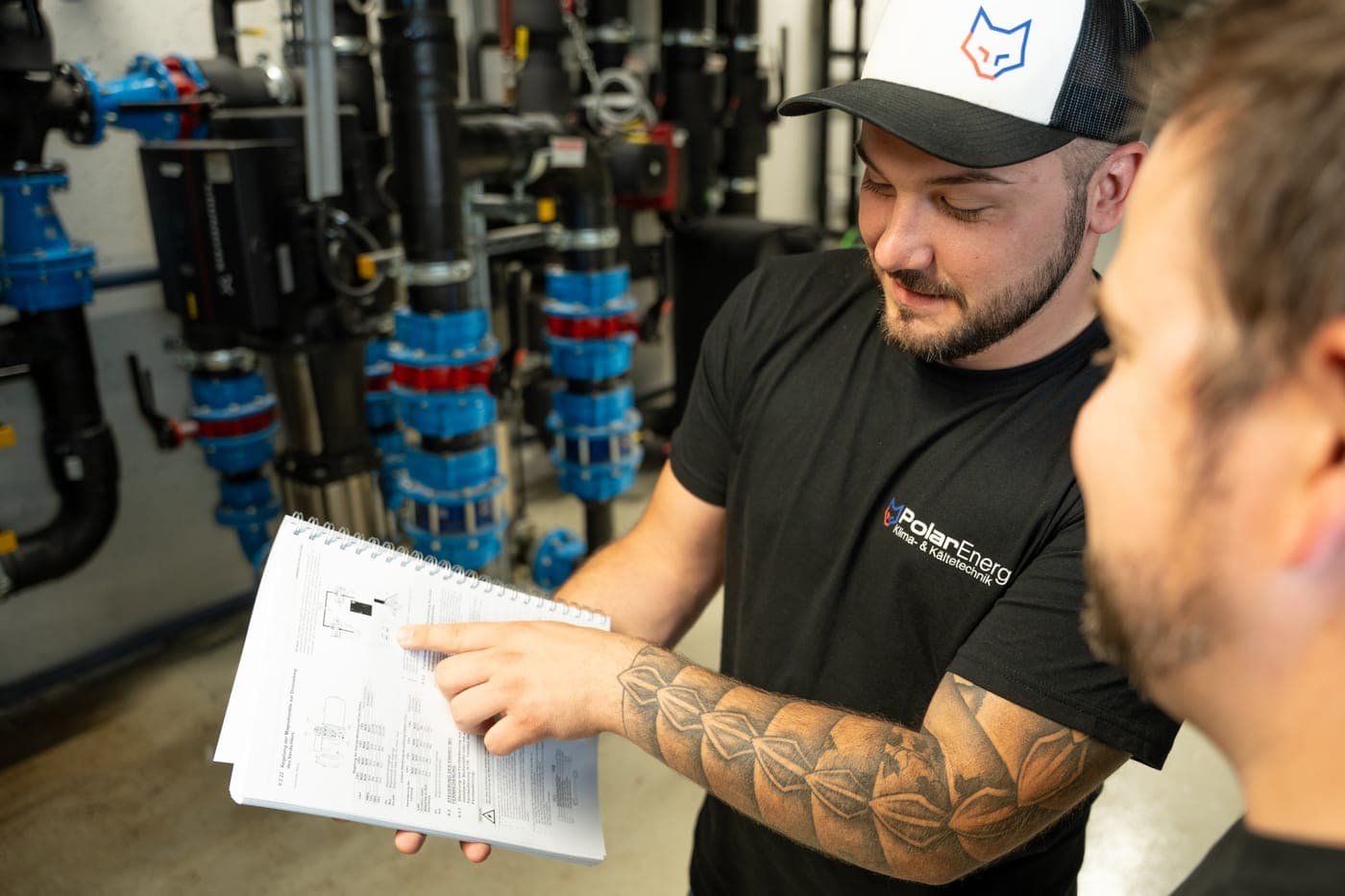 Zwei Techniker von Polar Energy besprechen den Anlagenplan vor blauen Absperrventilen