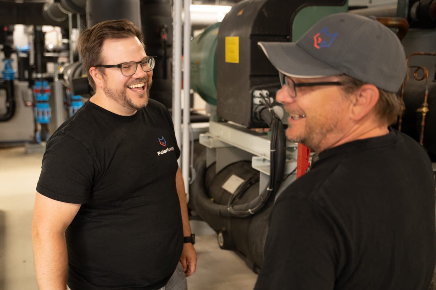 Zwei Polar-Energy-Techniker lachen gemeinsam im Technikraum